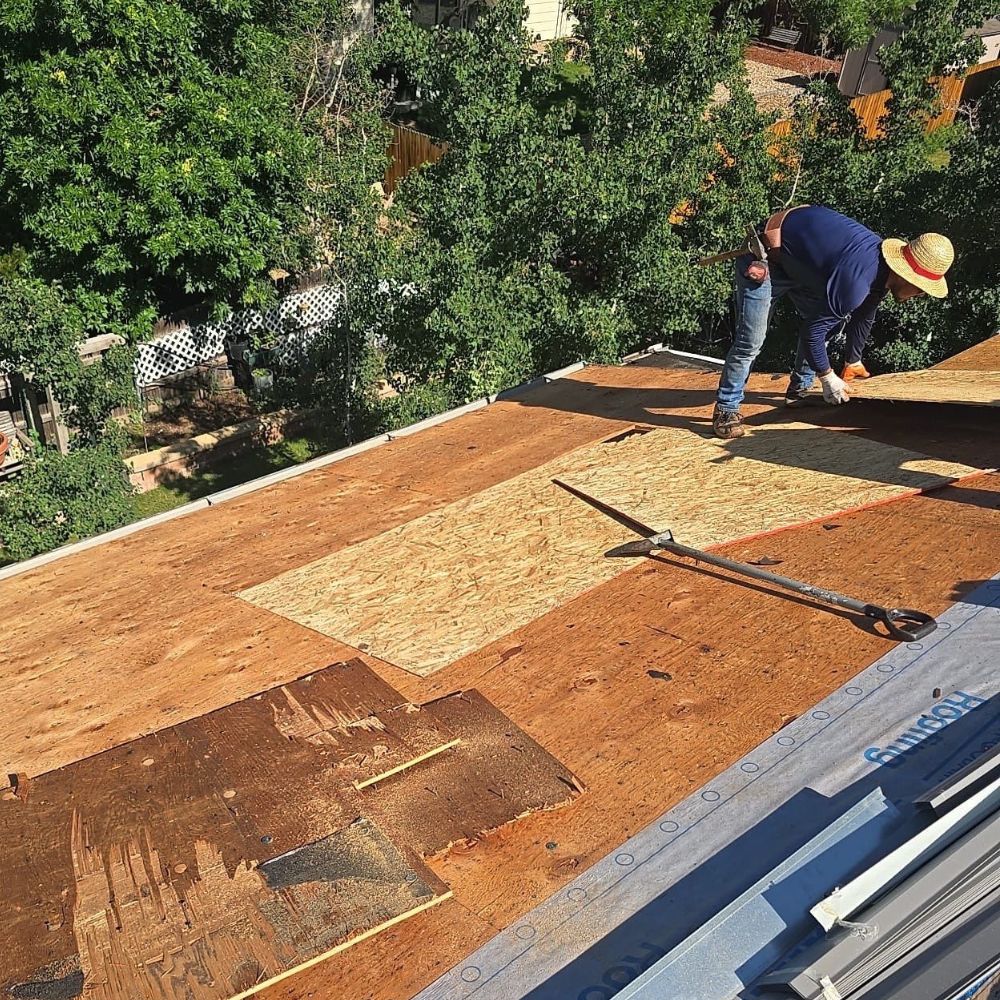 roofer replacing damaged plywood decking during roof tear-off and structural repair