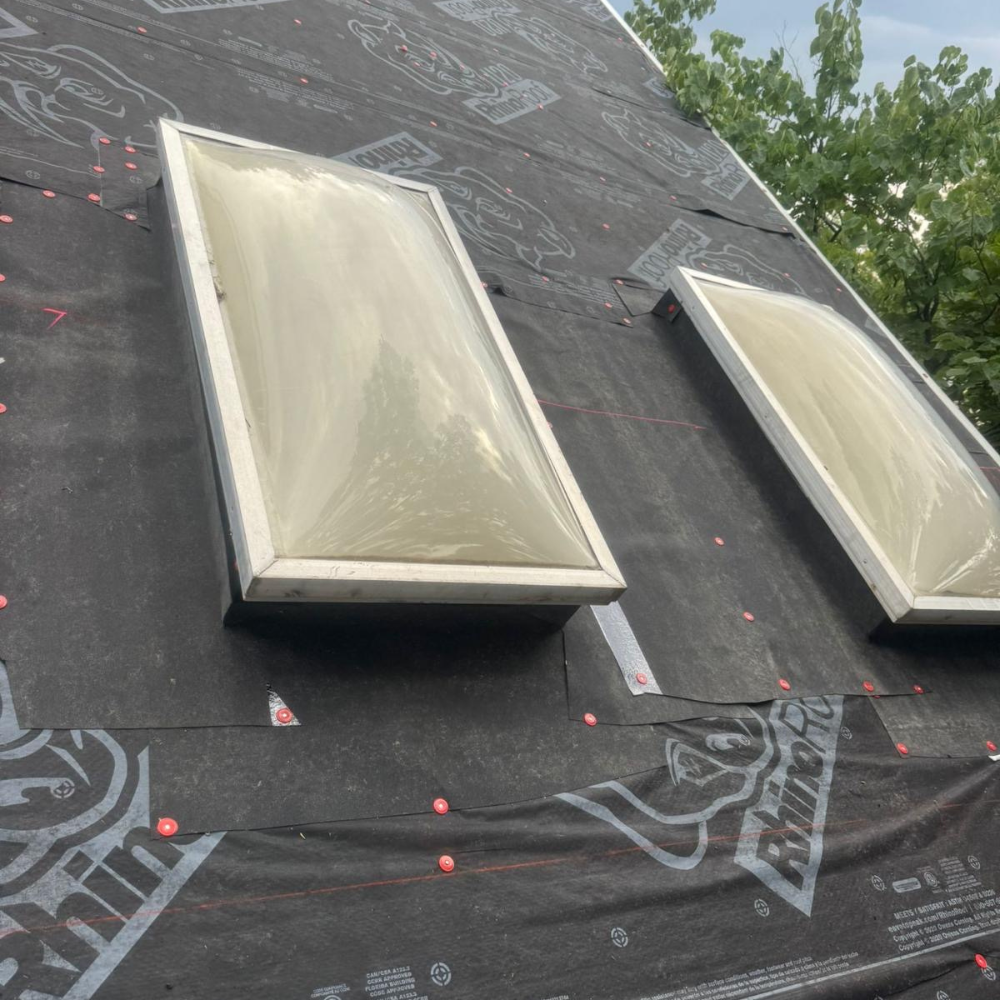 A pair of aged skylights resting on roofing underlayment during removal and replacement.